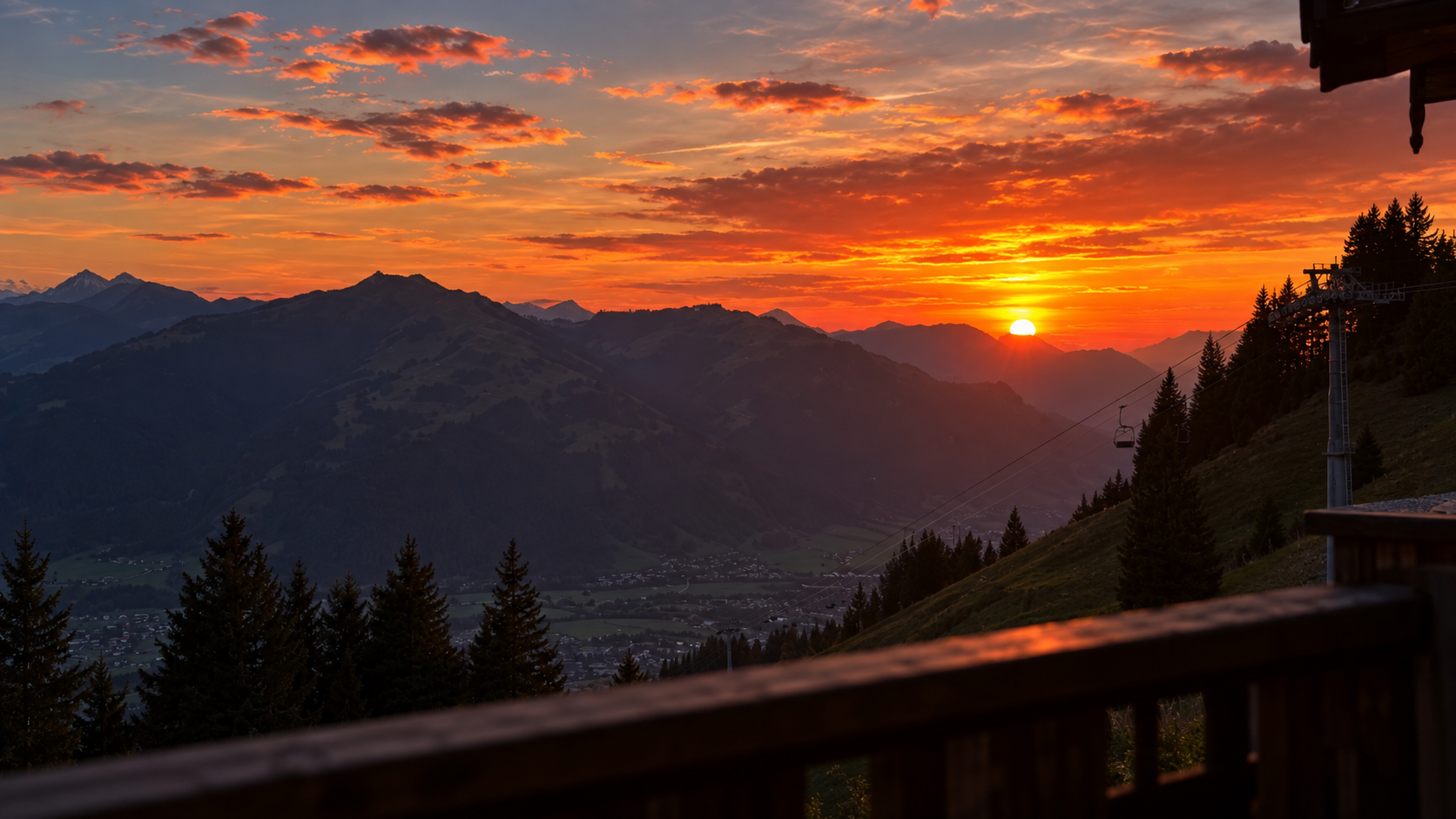 Roter Sonnenuntergang über einer Alpen-Felskette, im Vordergrund ein dunkles Terrassengeländer.