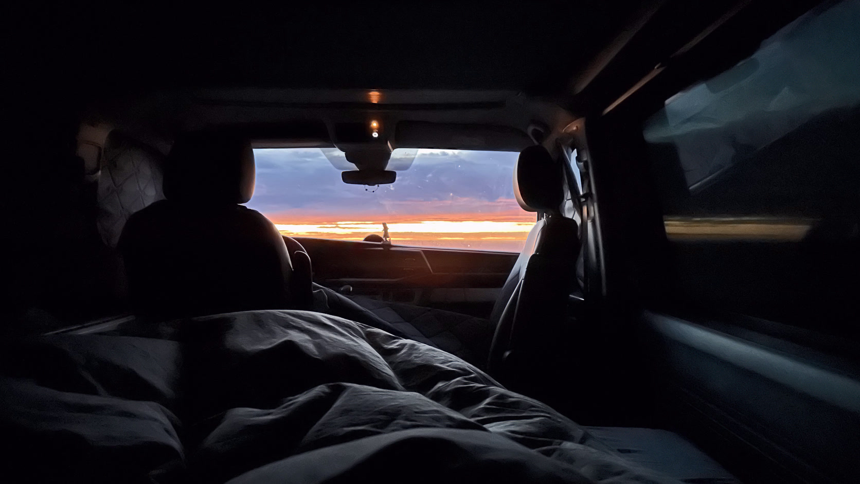 Blick aus dem Bett im Bus durch die Scheibe auf einen Sonnenaufgang.